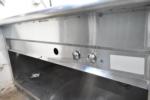 Stainless steel steam table with sneeze guard and under shelf, showing control knobs and shelf area, in used condition.