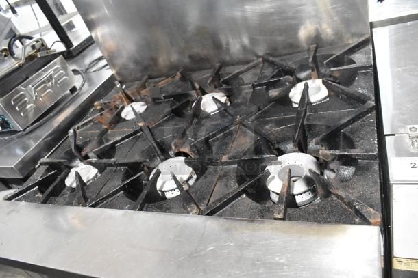 Sierra stainless steel commercial gas-powered 6 burner range with oven, over shelf, and back splash. Used condition.