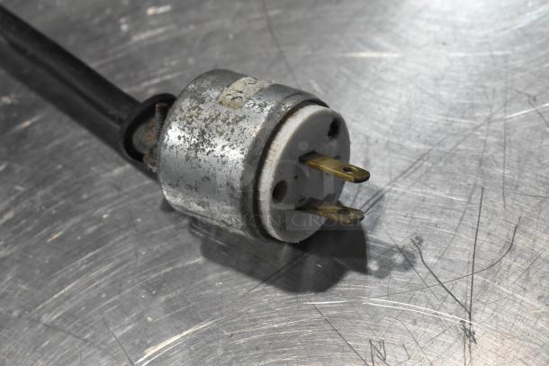 Rusty electrical plug attached to a black cord, resting on a scratched metallic surface.