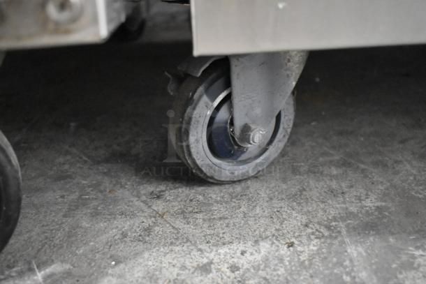 Stainless steel undercounter cooler caster, showing sturdy commercial design on a concrete floor.
