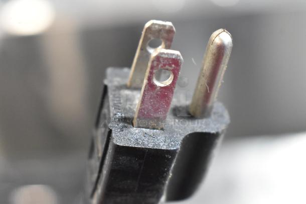 Close-up of a 115-volt plug for a commercial 3 hopper slushie machine, highlighting prongs and electrical connection.