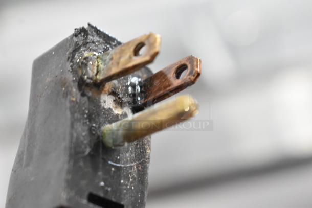Close-up of a worn plug with three metal prongs; one prong appears rusty. The plug is part of an ice cream dipping cabinet.