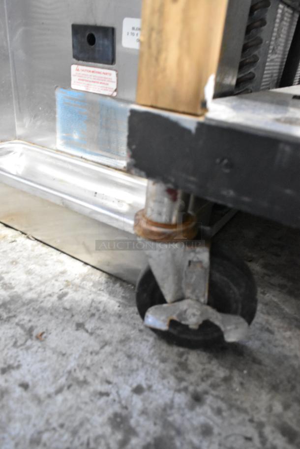 Stainless steel 4-bay steam table with under-shelf on casters, features storage and mobility. Visible warning label.