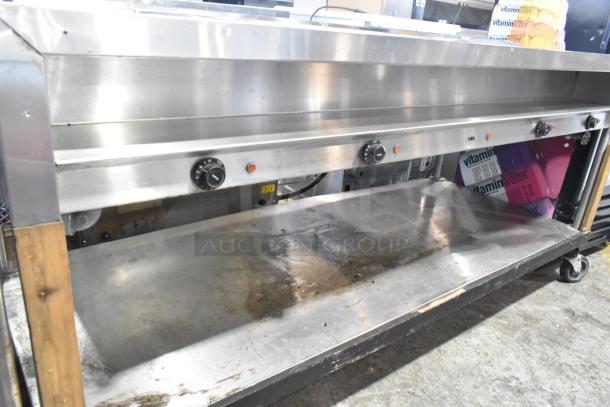 Stainless steel 4 bay steam table with under shelf, commercial casters, control knobs; visible wear, ideal for food service.
