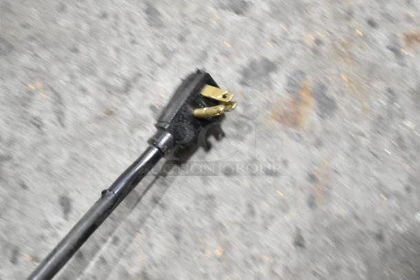 Blurry image of a black power plug with three prongs on a gray, speckled background.