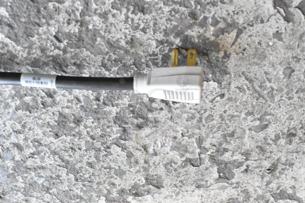 White electrical plug with visible barcode label on a textured gray stone surface.