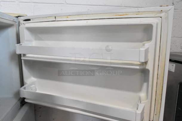 Whirlpool W1TXNMFWQ00 metal cooler with freezer, showing interior door shelves. Used condition, some wear visible.