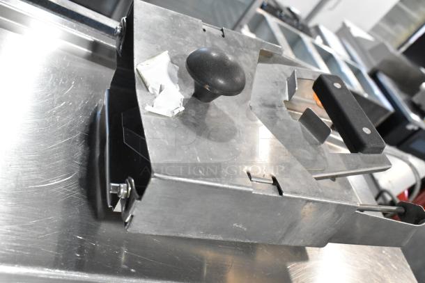 Stainless steel device with black handle and knob, used for slicing or processing, shown on metallic surface.