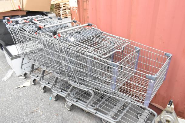 Five metal shopping carts in used condition, stacked together. Features sturdy wire frames and rolling caster wheels.