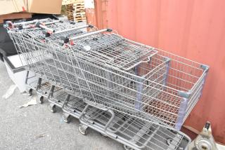 Five metal shopping carts in used condition, stacked together. Features sturdy wire frames and rolling caster wheels.