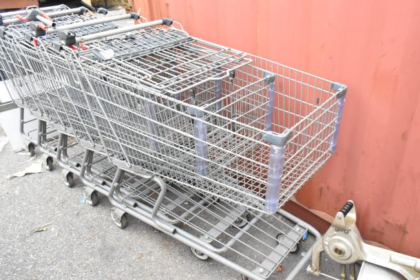 Five metal shopping carts in fair condition, stacked together, featuring durable wireframe design and swivel casters.