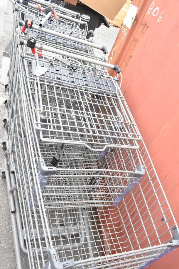 Five clustered metal shopping carts, sturdy condition, equipped with infant seats and safety straps, suitable for retail use.