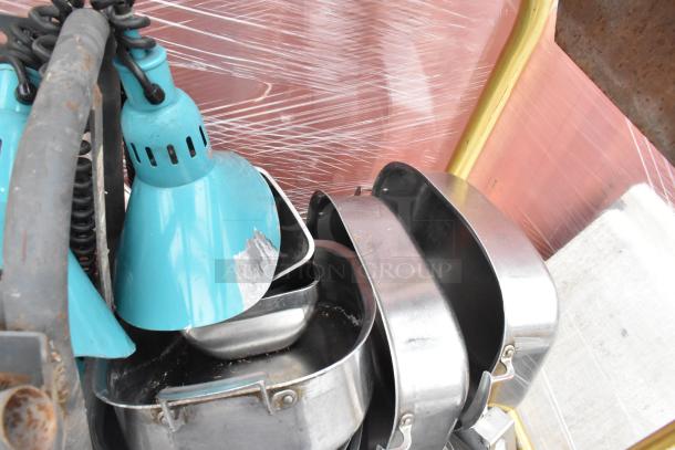 Metal luggage cart with commercial casters, containing metal baking pans and a poly trash can, showing some wear.