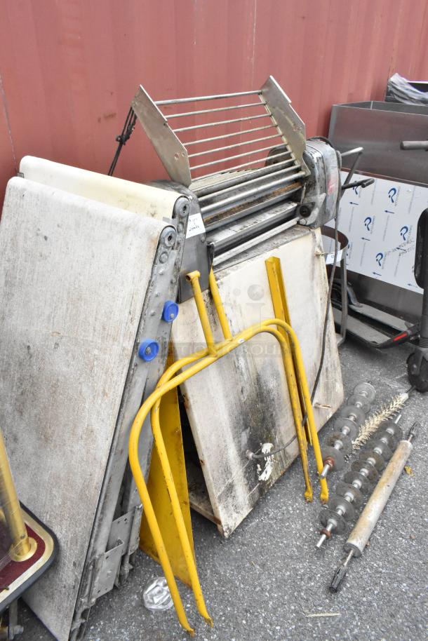 Rondo Seewer metal commercial dough sheeter, partially disassembled, possibly missing parts, seen outdoors.