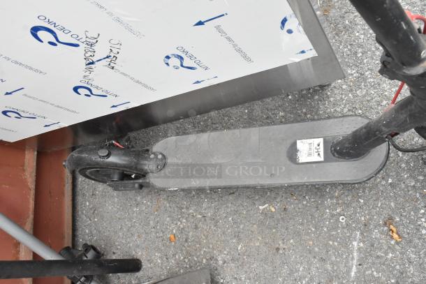 Two black scooters on pavement, each with wear, featuring a deck label and visible wiring.