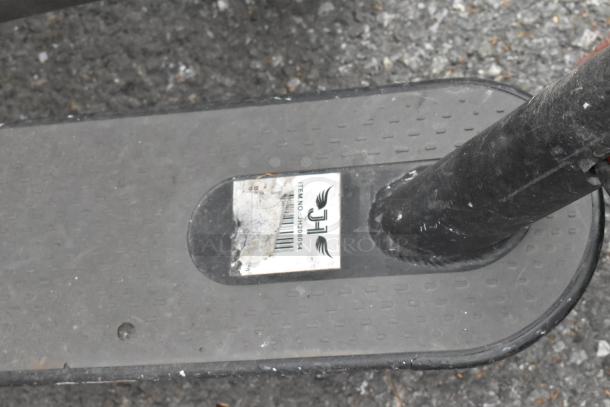 Close-up of a black scooter footboard showing a label with the item number JH280854. Board has a textured surface.
