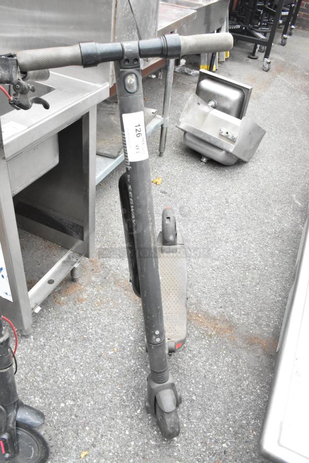 Two black Segway scooters with visible wear, displayed outdoors. Handle grips and baseboard details shown. Tag reads "126 WR2."