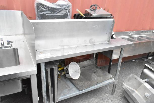 Stainless steel table with metal under shelf, shows signs of wear. Includes miscellaneous contents underneath.