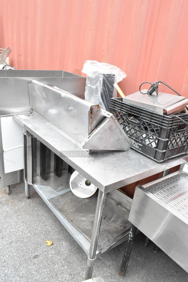 Stainless steel table with metal under shelf, includes various contents. Shows signs of use, suitable for industrial kitchens.