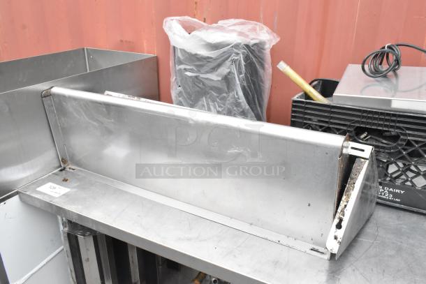 Stainless steel table with metal under shelf, showing visible wear and rust. Includes assorted contents on and around the table.