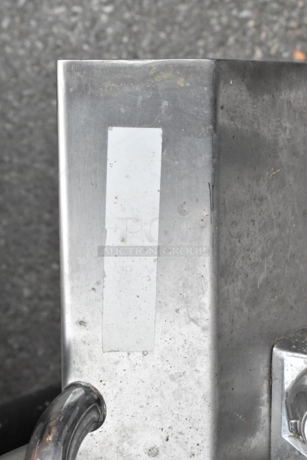 Stainless steel single bay sink corner showing a faucet handle, slight surface wear, and an attached label.