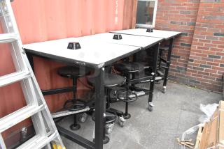 Three industrial tables with attached black stools, silver frames, and caster wheels. Sizes include 30x36x46 and 51x36x46.