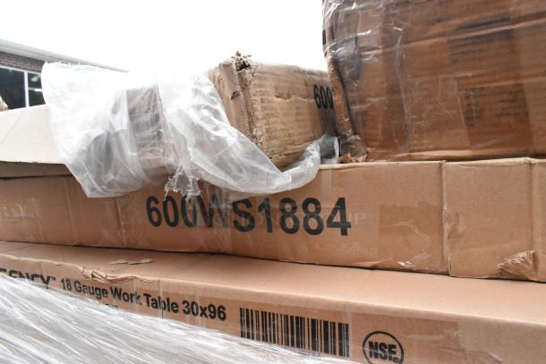 Cardboard boxes labeled "600WS1884" containing scratch and dent stainless steel tables. Boxes show visible wear.