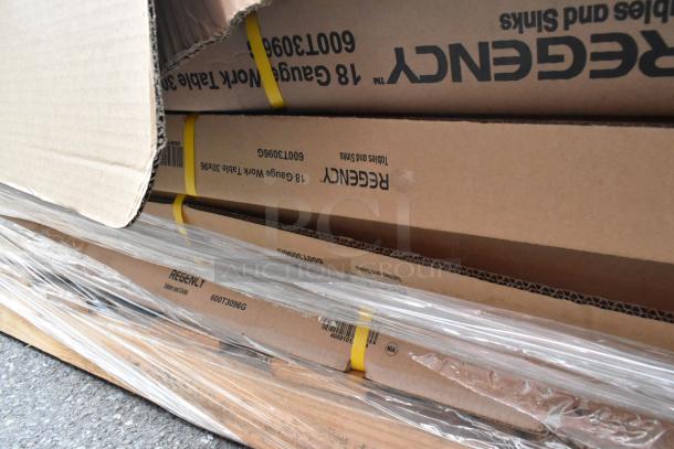 Cardboard boxes labeled "Regency" containing new stainless steel tables with minor scratches, secured in plastic wrapping.