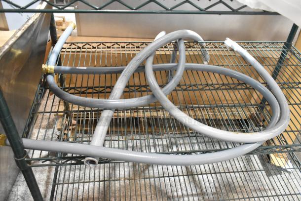 Two-tiered metal shelving unit with coiled grey hoses and brass fittings, in used condition.