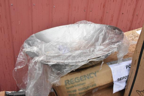 Stack of boxes labeled "Regency" with a stainless steel wok, wrapped in plastic, atop. Boxes show dents.