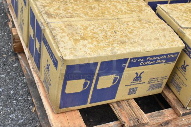 Box labeled "12 oz. Peacock Blue Coffee Mug" with visible wear on the cardboard, resting on a pallet.
