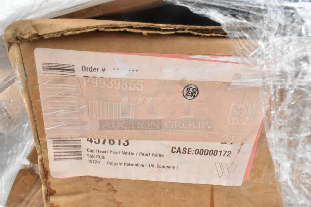 Cardboard box with visible scratches and dents, label reads "Cap Heart Pearl White," 550 pieces, Colgate-Palmolive.
