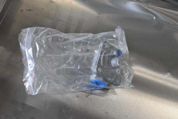 A small metal component sealed in a clear plastic bag, on a stainless steel surface.