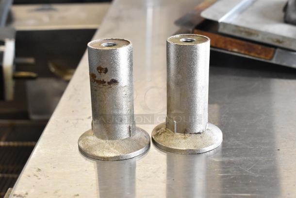 Two metal cylindrical components, possibly commercial oven parts, with some rust spots, on a stainless steel surface.