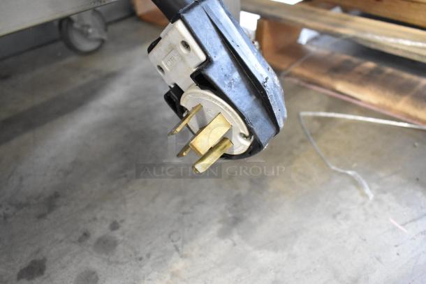 Close-up of a power plug connected to a Turbochef HhC2020 commercial pizza oven, showing prongs and casing.