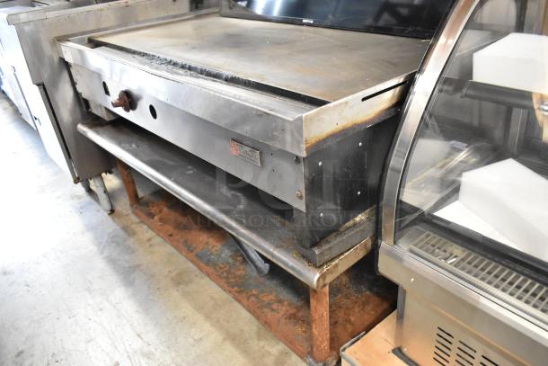 Wolf stainless steel commercial gas griddle on a stand, showing slight wear; features durable flat top and visible brand logo.