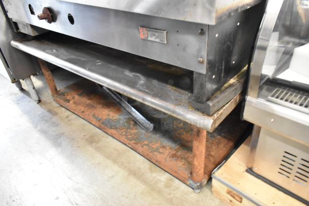 Wolf stainless steel commercial countertop gas griddle on equipment stand, visible wear, rusting stand, Wolf logo prominent.