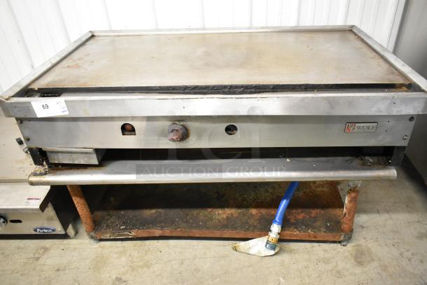 Wolf stainless steel commercial countertop gas griddle on stand, visible wear, branded logo, utility connection attached.