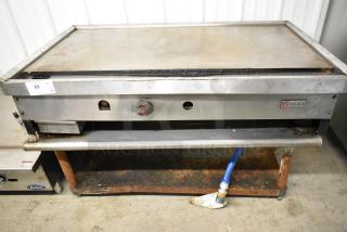 Wolf stainless steel commercial countertop gas griddle on stand, visible wear, branded logo, utility connection attached.