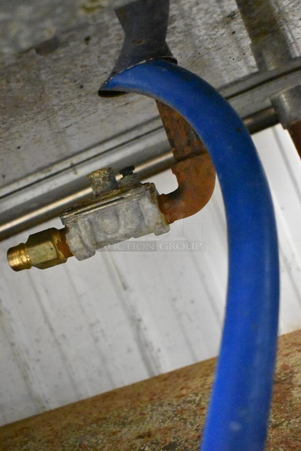 Gas connection beneath Wolf stainless steel commercial flat top griddle, showing blue hose and metal fittings.
