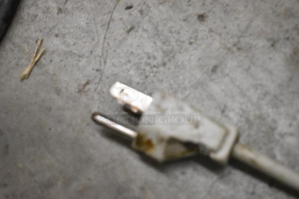 Blurred close-up of a power plug on a gray surface, unclear details. Related to Sam4s ER-5215M Cash Register.