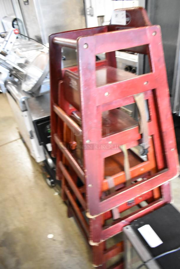 Stacked set of four Winco wooden high chairs in used condition, showing red finish and safety straps.