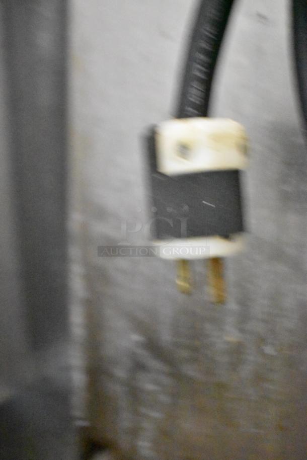 Blurry image showing a power plug connected to an Alto Shaam 500-TH/III Cook N Hold Cabinet, indicating it's powered electrically.