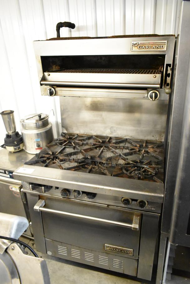 Garland stainless steel 6-burner range with oven, salamander cheese melter, and backsplash. Used condition, visible branding.