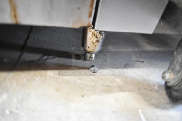 Garland stainless steel commercial 6-burner range with oven, salamander cheese melter, and back splash, showing a rusted leg.