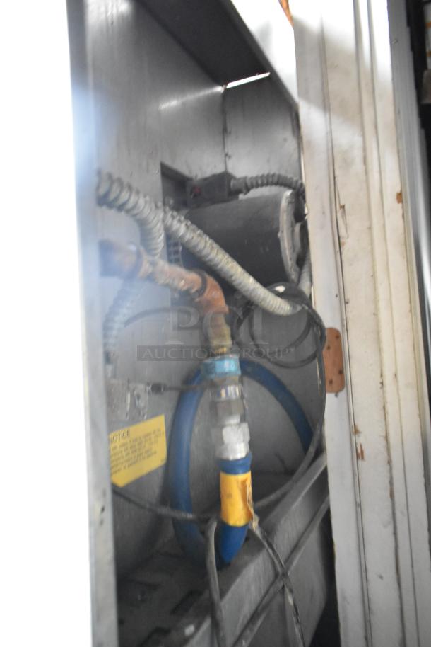 Interior view of a Bakers Pride gas-powered convection oven showing blue gas hose, metal fittings, and wiring.