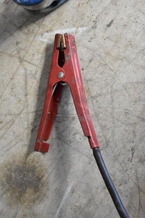Red clamp from Schumacher SE 8050 Battery Charger, showing moderate wear, attached to a black cable.