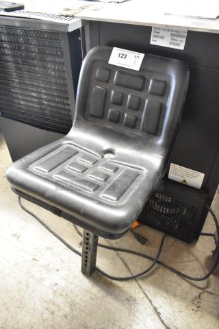 Black exercise bicycle seat with textured surface, mounted on an adjustable post. Label shows auction number 123.