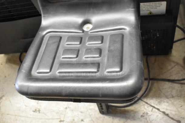 Black exercise bicycle seat, slightly worn, with a textured grid pattern and a central white mounting hole.