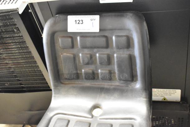 Black exercise bicycle seat with square pattern design, auction tag number 123 attached. Appears in used condition.